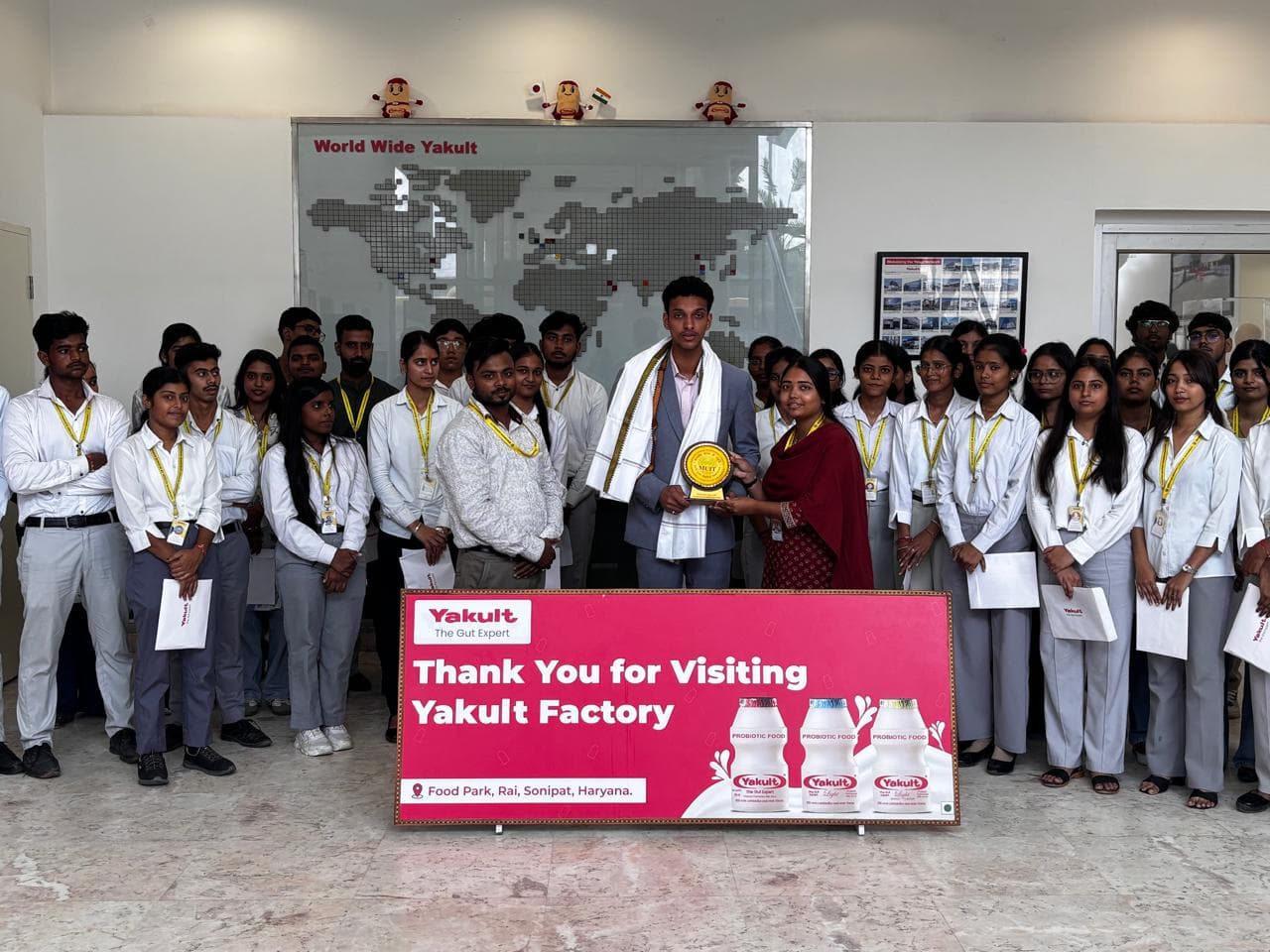 Faculty presenting a memento to the Yakult host in front of the World Wide Yakult map